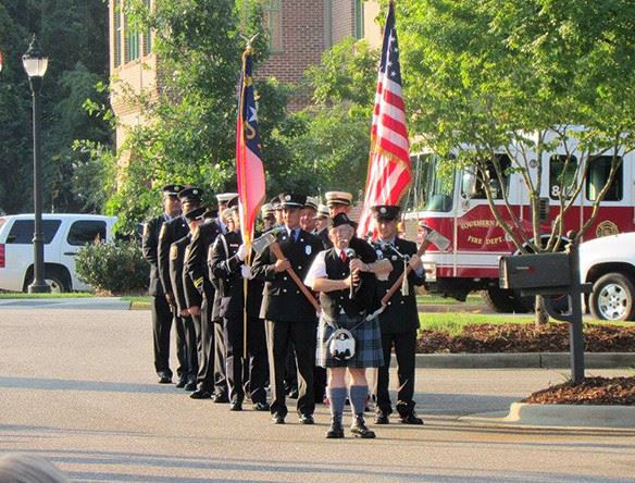A man playing a bag pipe followed by men in uniform with an american flag